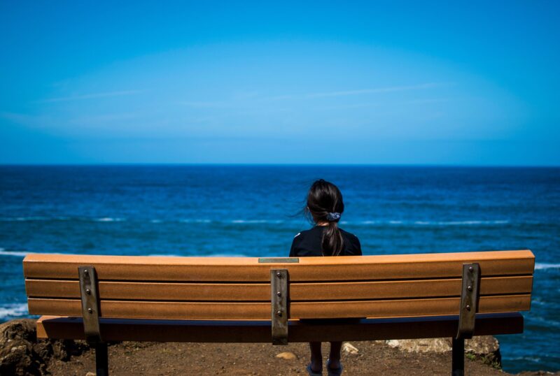 ベンチに座って海を眺める女性