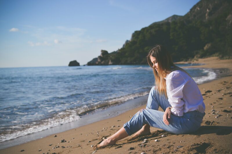 海辺の砂浜に座って物思いにふける女性